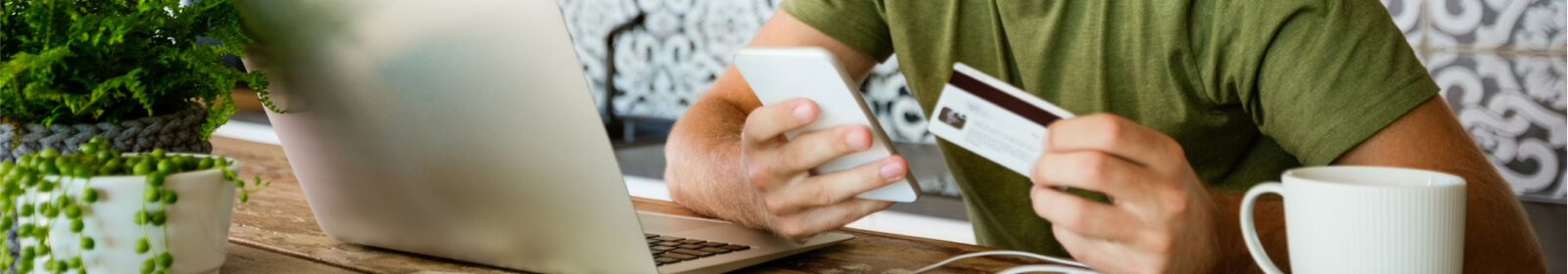 Person in front of a laptop holding their phone and credit card.